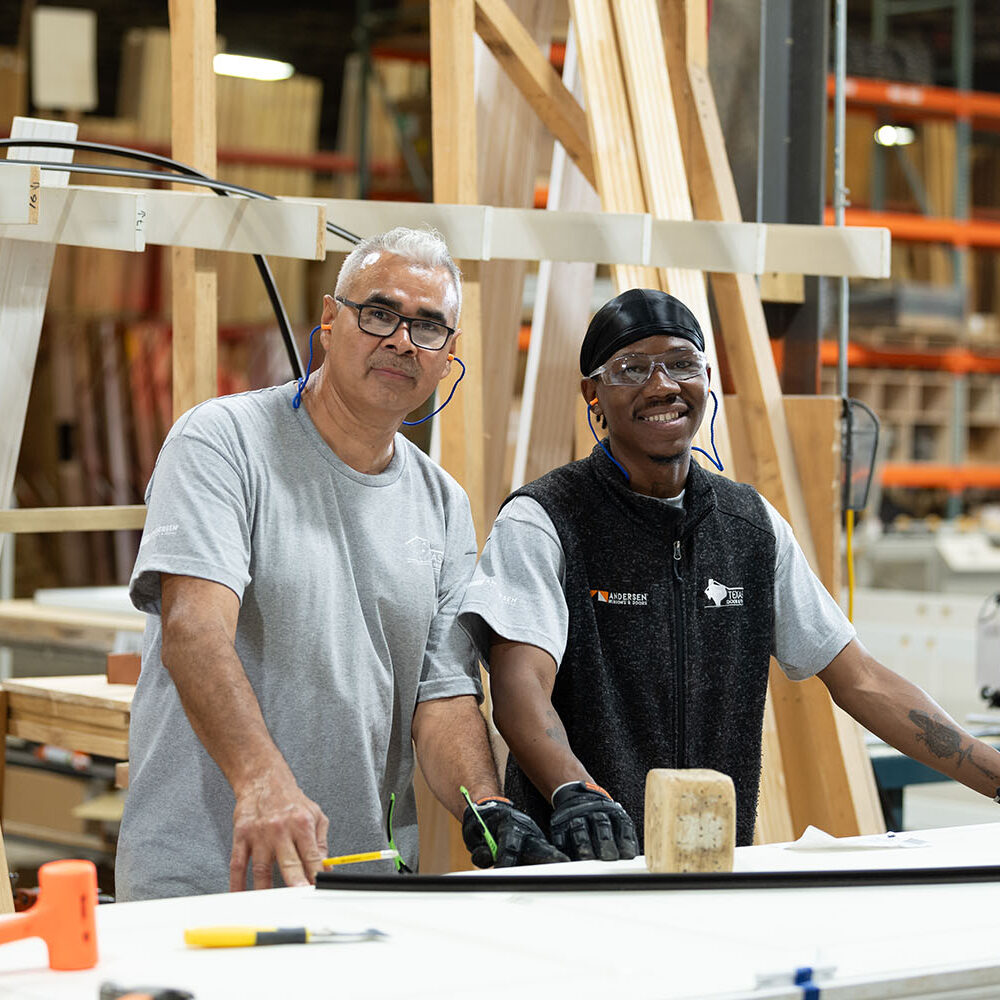 Two men smiling inside a millwork shop with hands on top of the workbench.